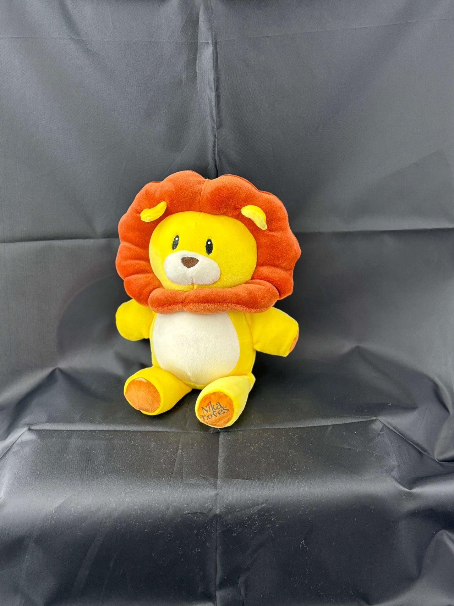 Plush lion toy with orange mane against a black background