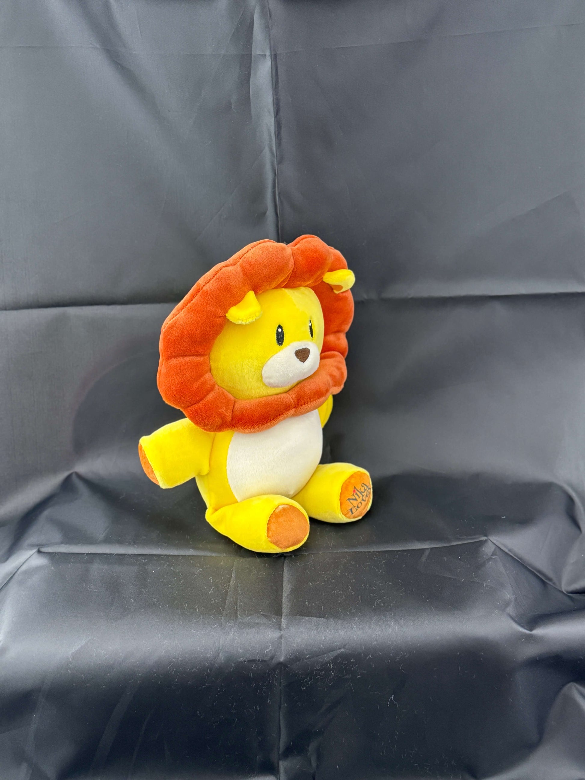 Cute yellow lion plush toy with an orange mane sitting on a black surface.