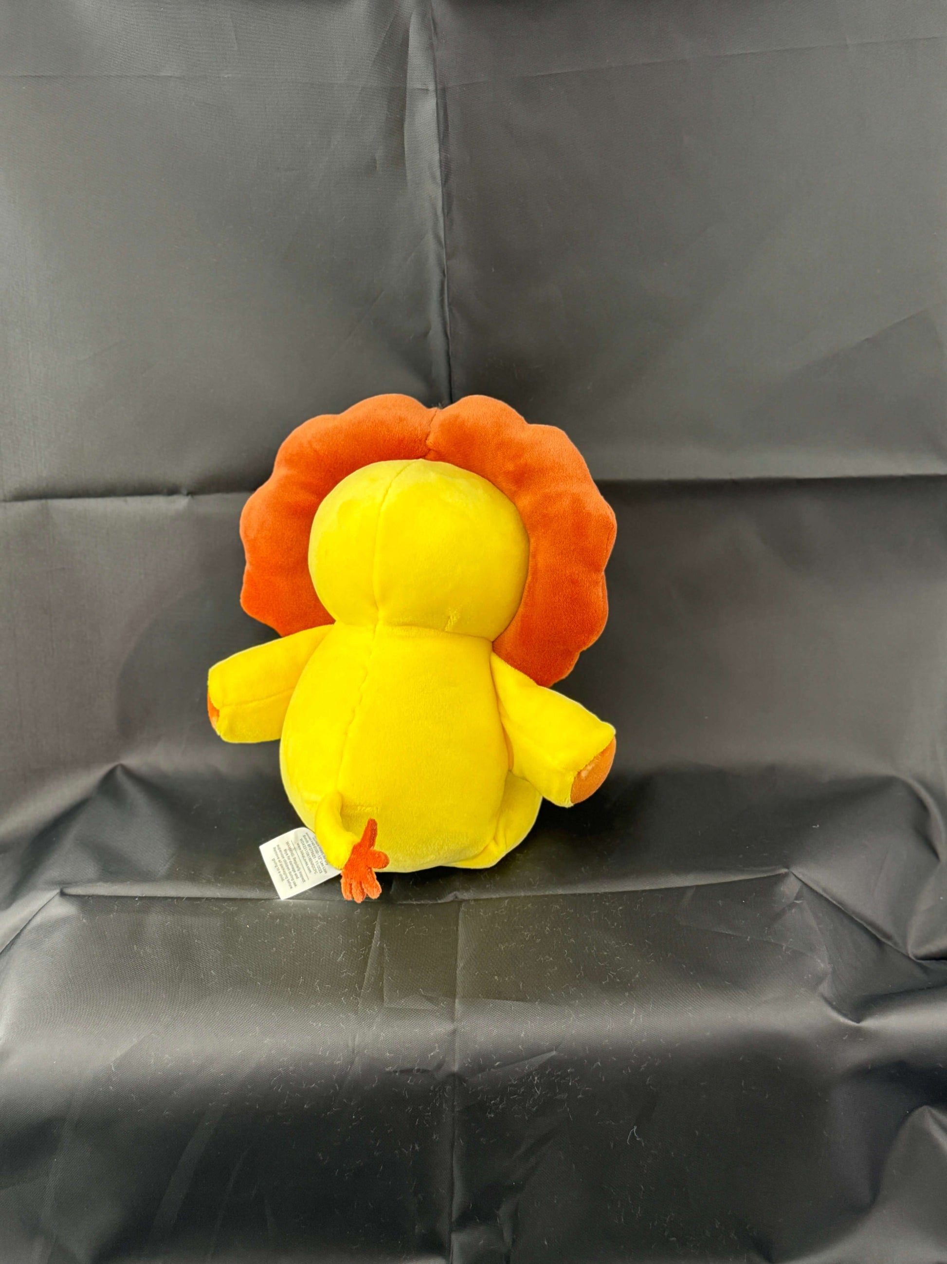 Yellow plush toy lion with orange mane on a black background