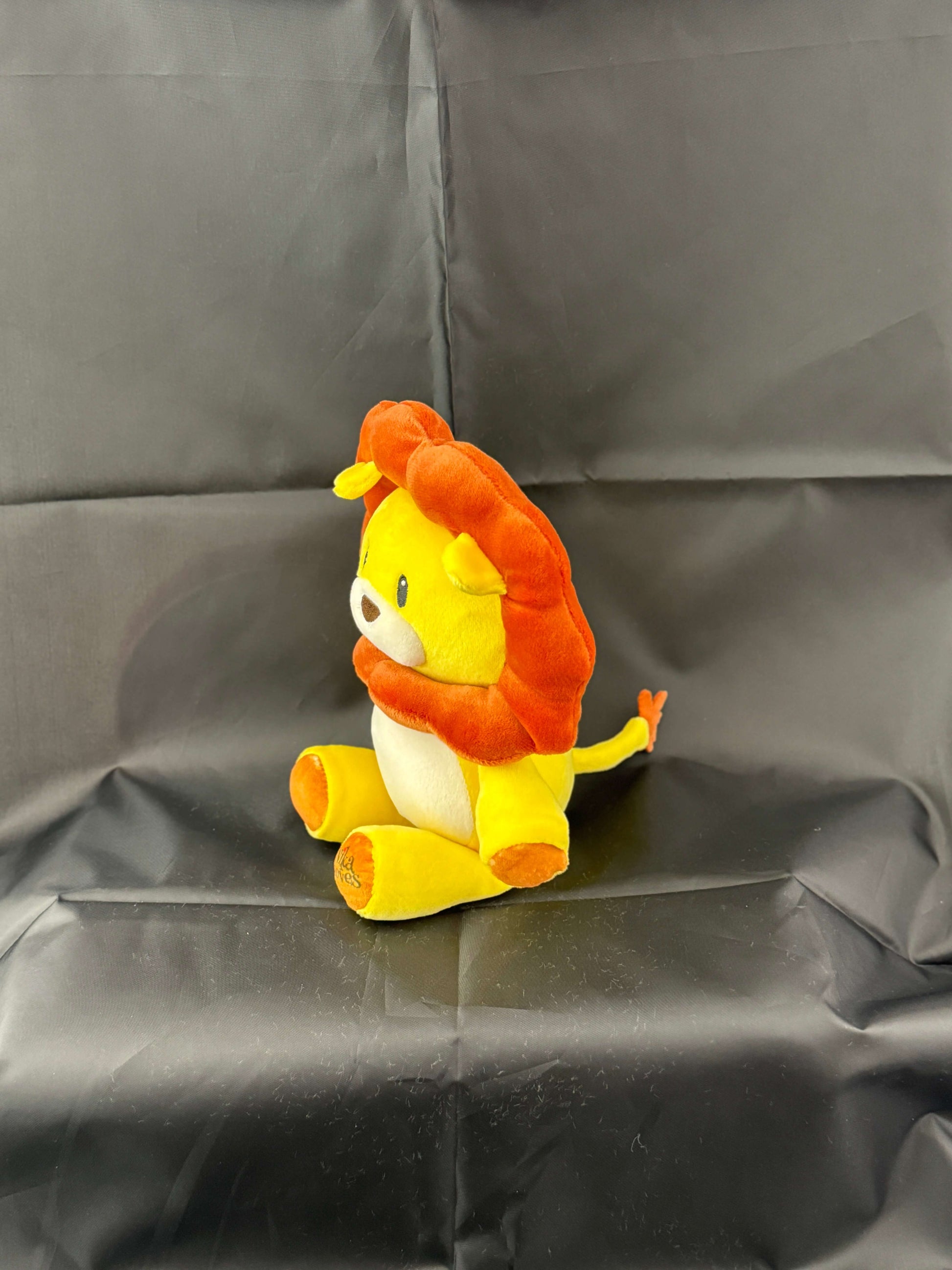 Stuffed lion toy with orange mane and yellow body sitting on a black background.