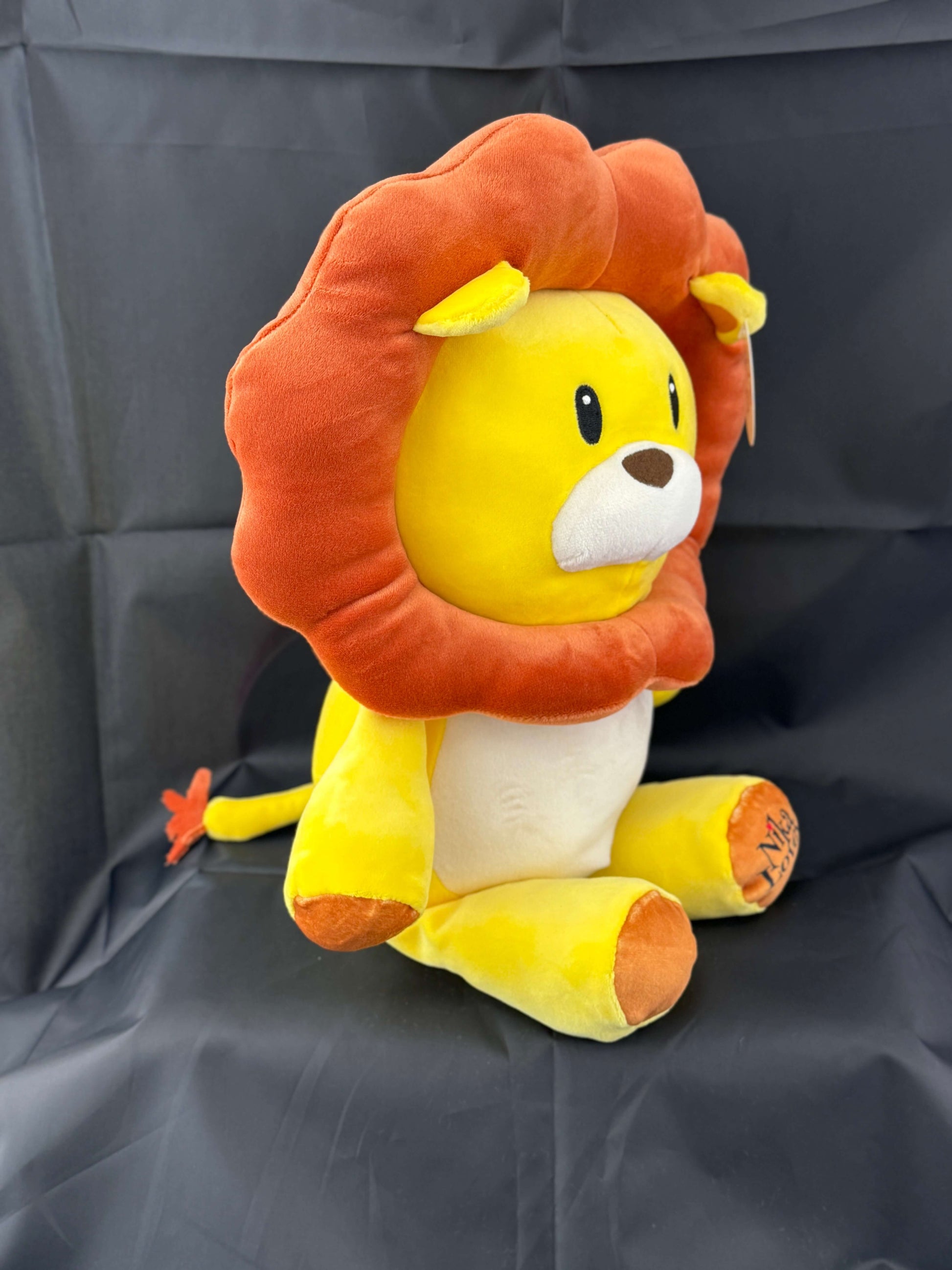 Cute yellow and orange lion plush toy sitting against a black backdrop