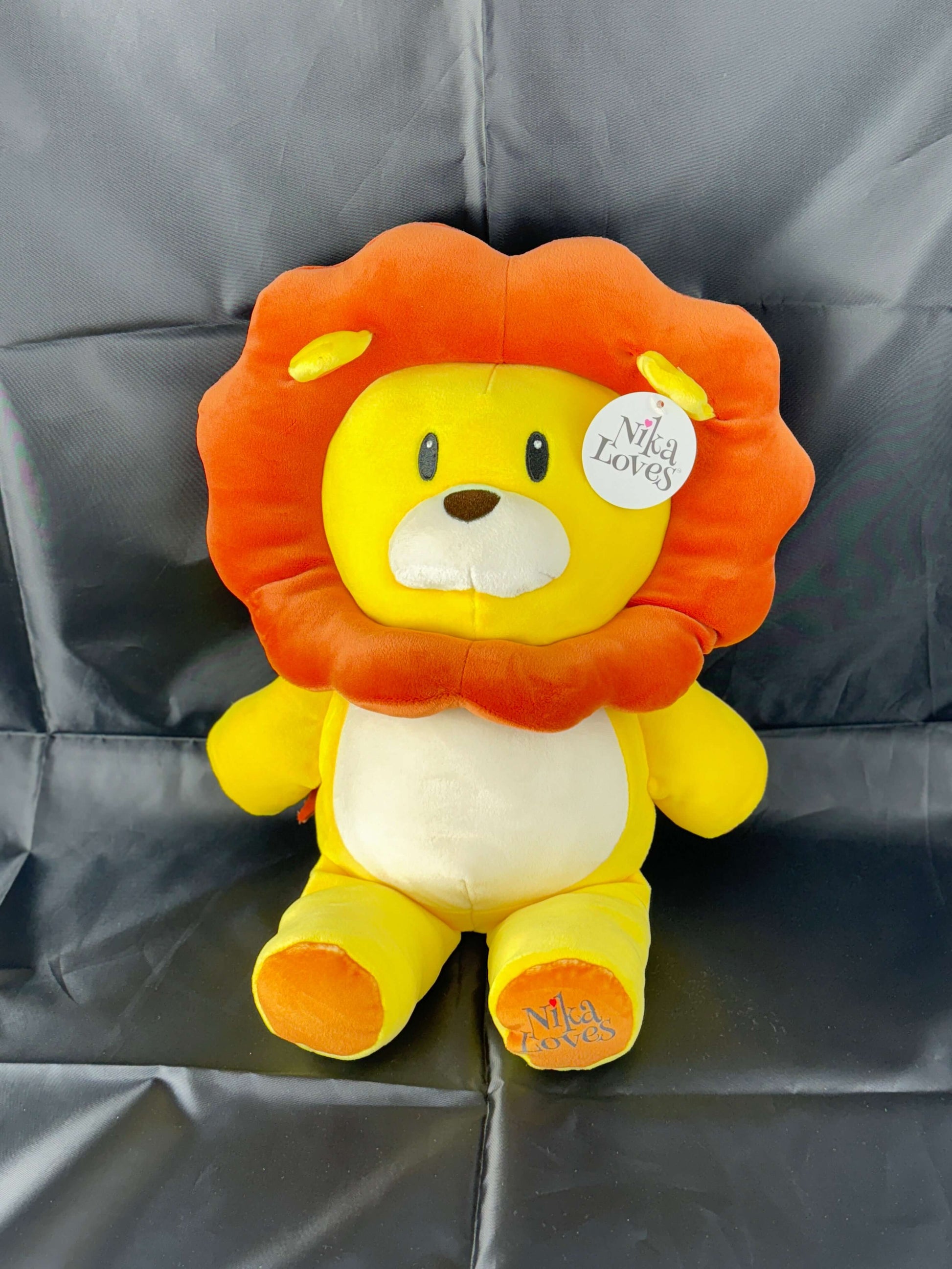 Plush lion toy with orange mane and yellow body sitting on a black backdrop.