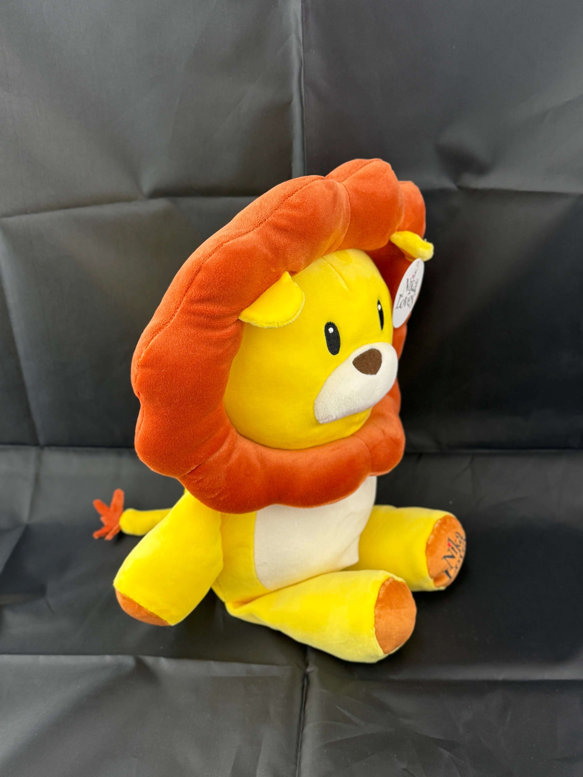 Plush lion toy with orange mane and yellow body sitting on a dark background.