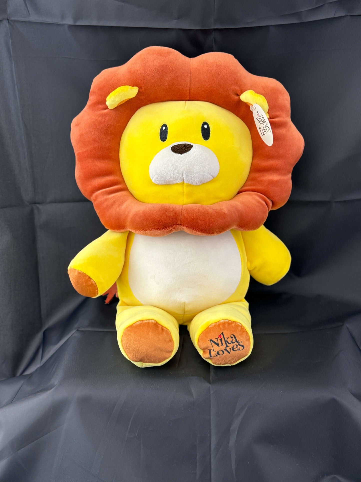 Plush lion toy with orange mane and yellow body sitting on a dark background, with "Niko Loves" stitched on its paw.