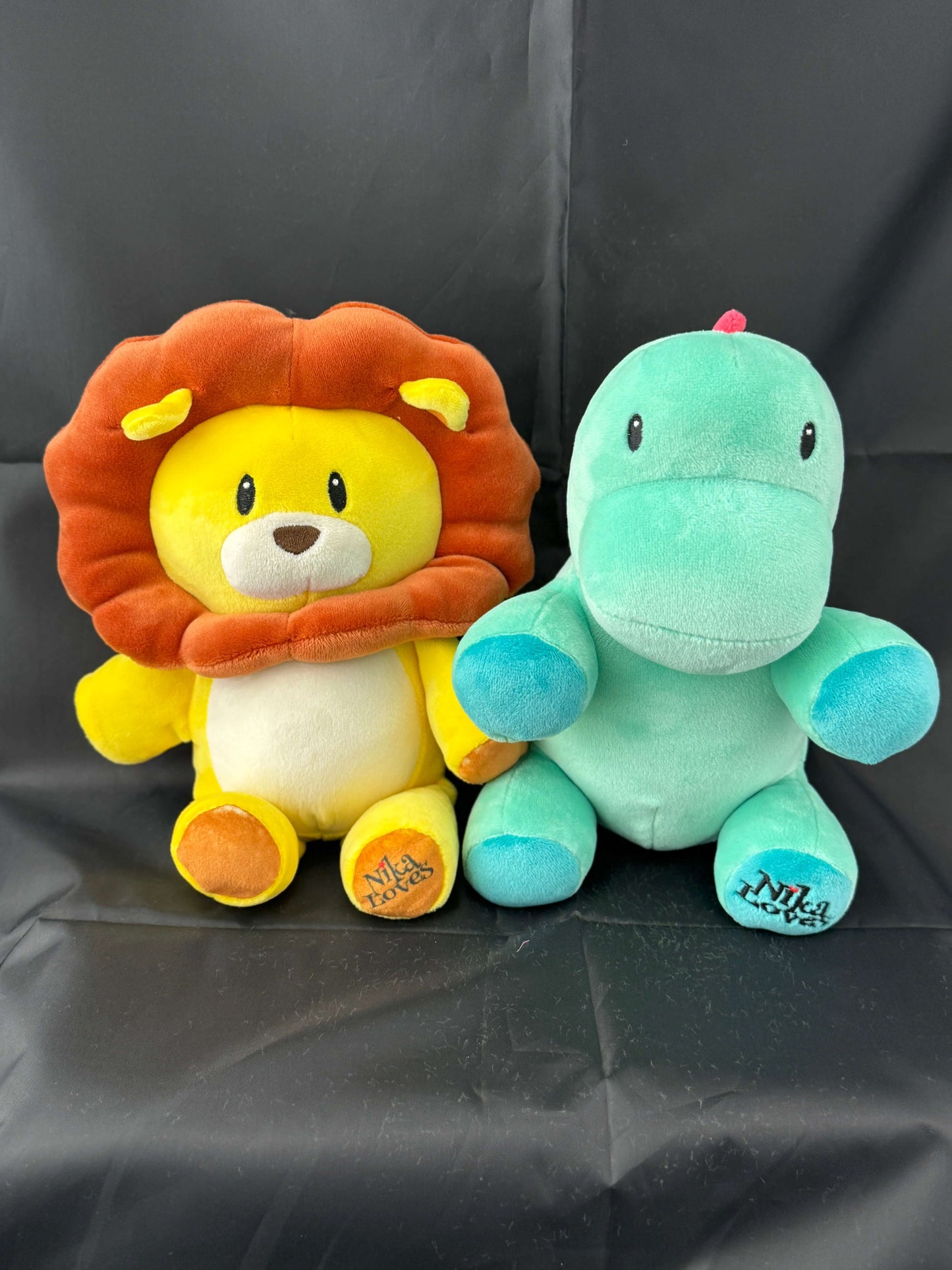 Plush lion and green dinosaur stuffed animals on a black background.