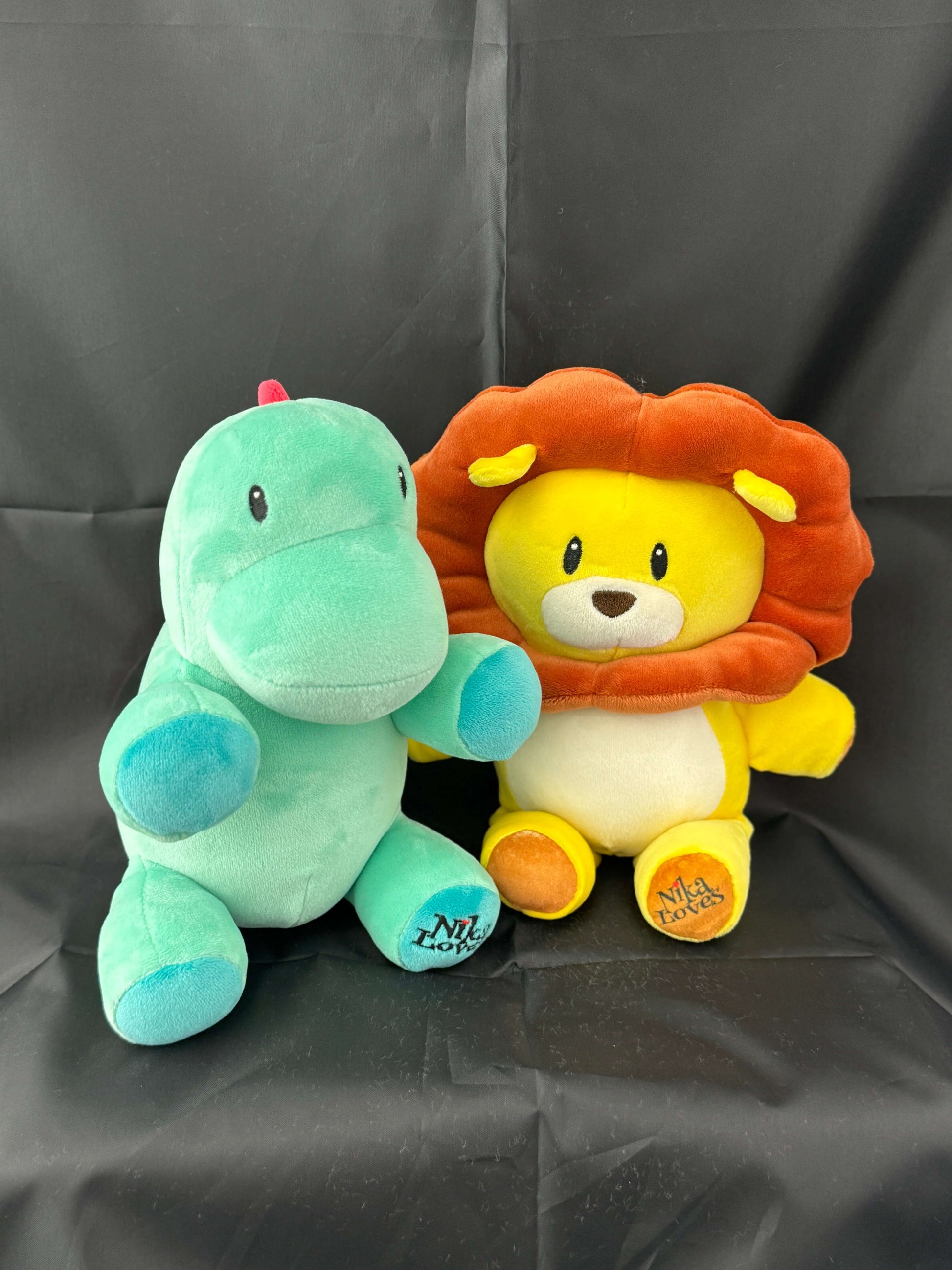 Green Genosaurus plush and yellow lion plush toy on a black background.