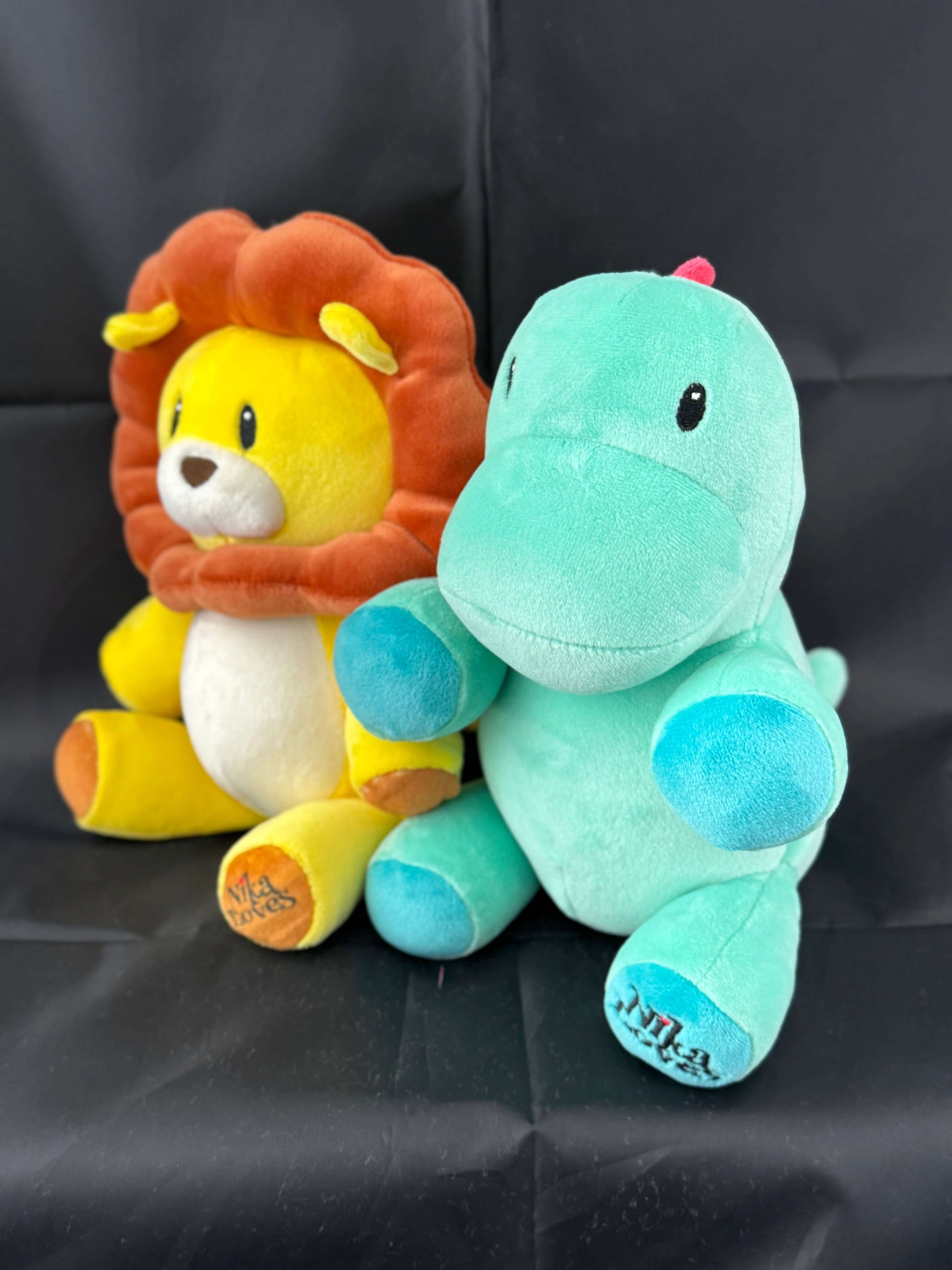 Yellow plush lion and green plush dinosaur toys on a black background.