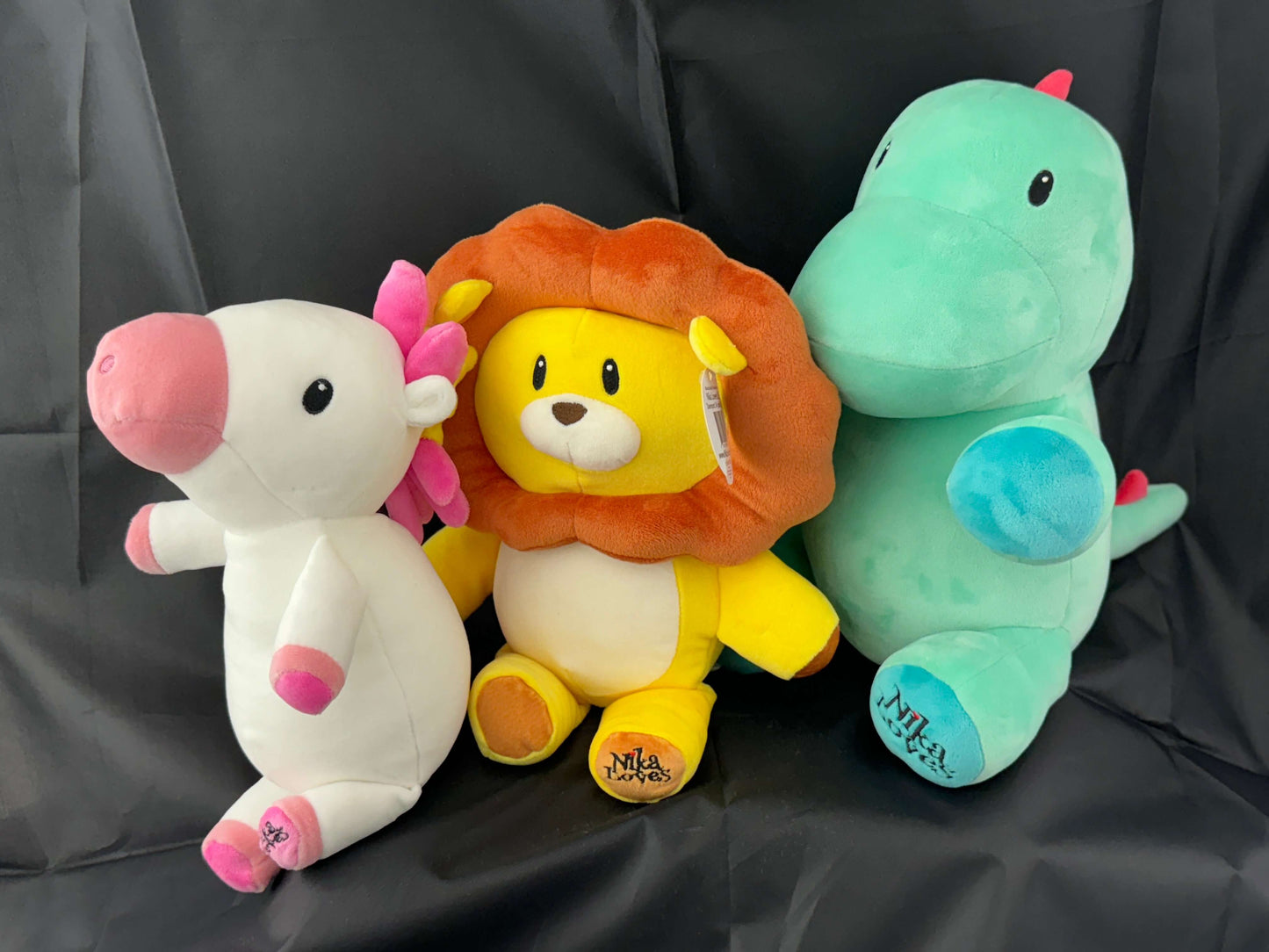 12" Leo the Lion plush stuffed animal with vibrant yellow body and detailed brown mane, surrounded by unicorn and dinosaur plush toys.