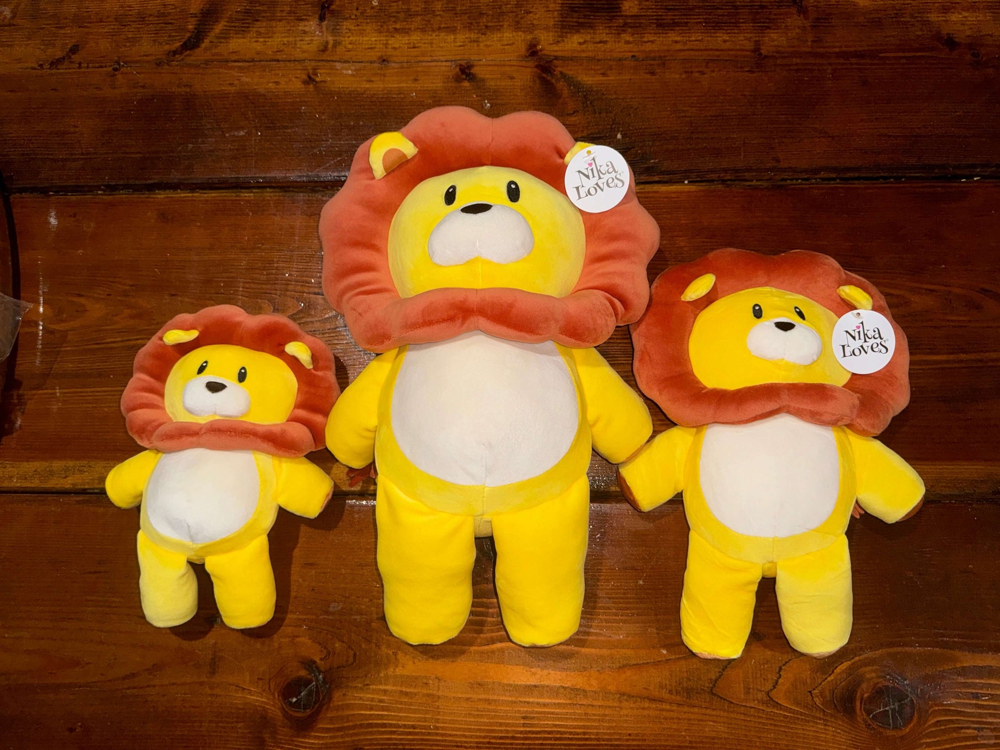 Three sizes of Leo the Lion plush stuffed animals from the "Nika Loves" book series, featuring vibrant yellow bodies and detailed brown manes.